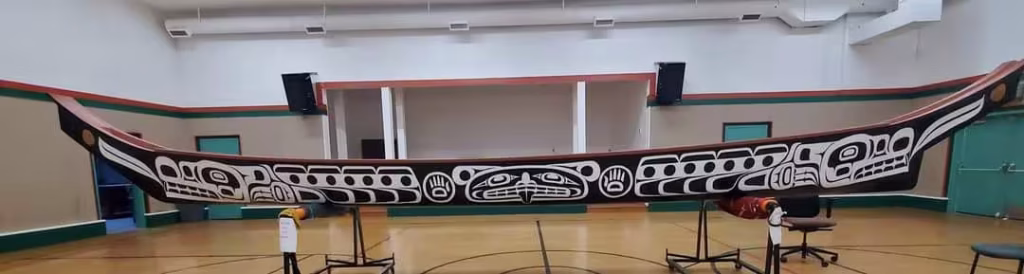 A side view of a large, carved K’ómoks First Nation canoe in a gymnasium