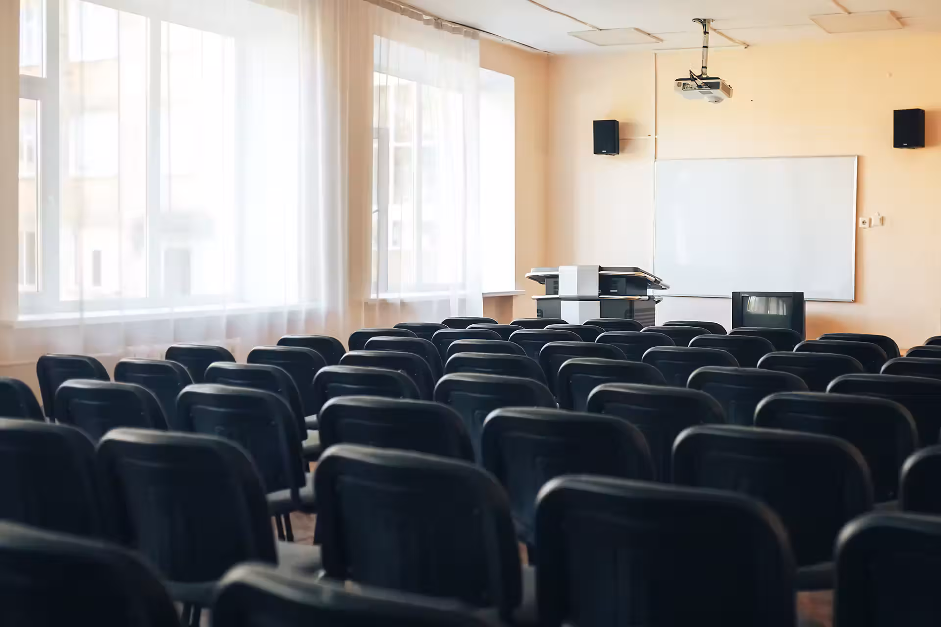 An empty classroom or lecture hall with rows of black chairs and a whiteboard