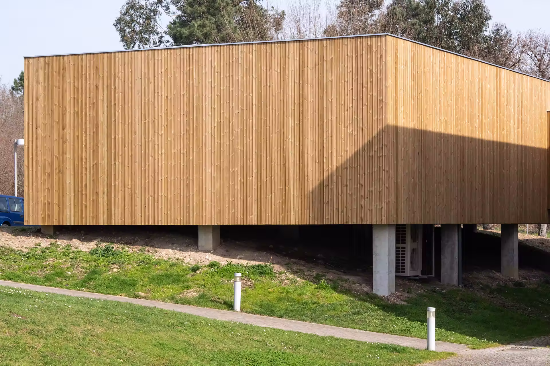 A modern rectangular building with vertical wood siding elevated on concrete pillars
