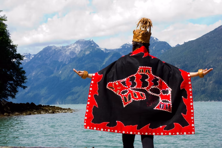 person wearing red and black cloak and cedar hat with welcoming arms outstretched