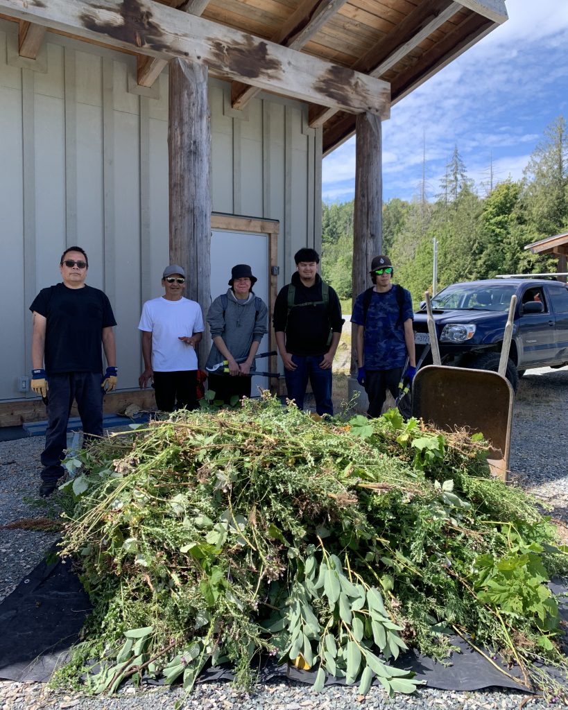Five people stand behind a large pile of pulled thistles and other vegetation.
