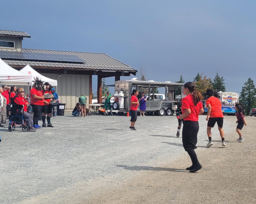 People in red shirts participate in an outdoor event near a building with solar panels.